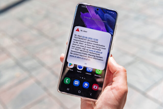Een telefoon in iemands hand met daarop het NL-Alert testbericht te zien.